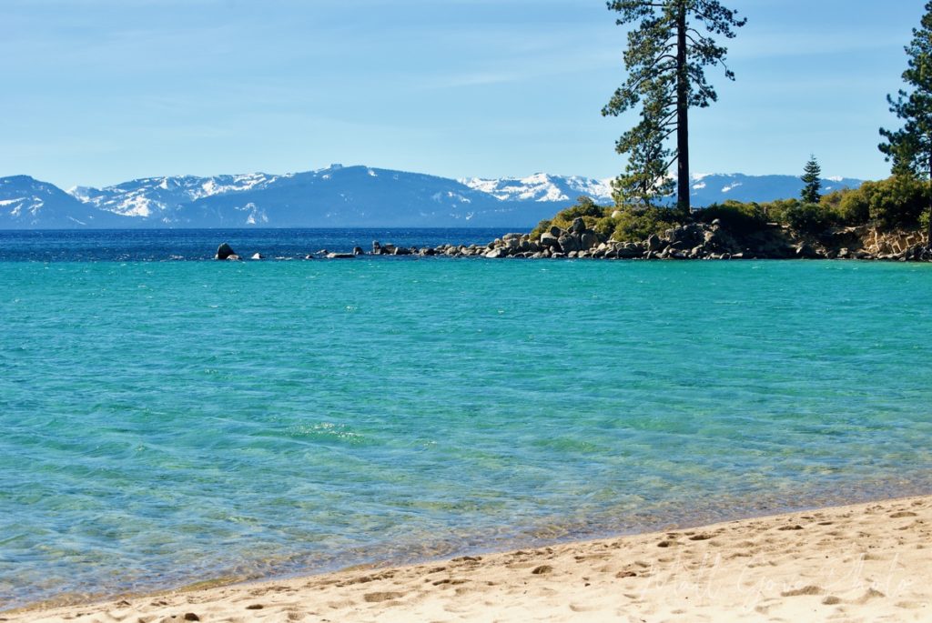 Crystal clear waters in a Lake Tahoe lagoon with the snow-capped Sierra Nevada providing a stunning backdrop.